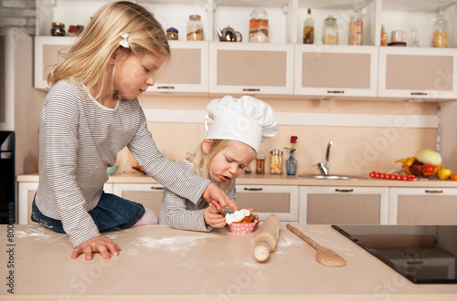 Little cute girls tasting cake in kitchen