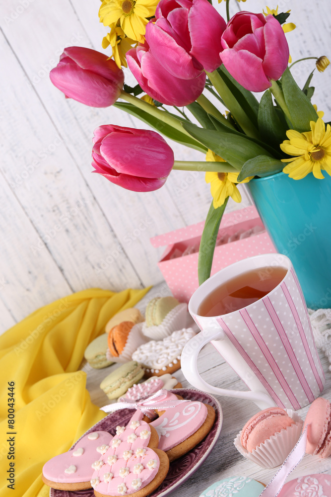 Composition of spring flowers, tea and cookies on table