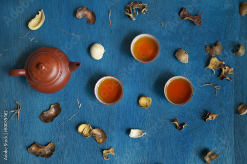 teapot and three cups with shuck on blue wooden table.
