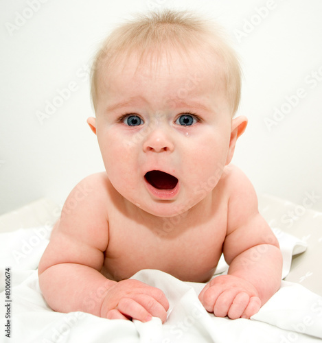 Crying 6 month toddler laying on a blanket on grey background
