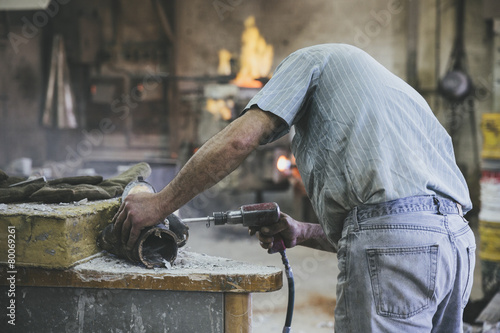 Man working with pneumatic drill on sculpture in a foundry
