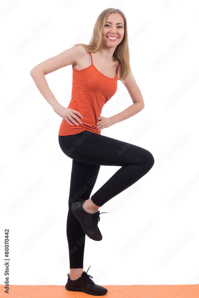 Smiling woman in sportswear training legs on a mat.