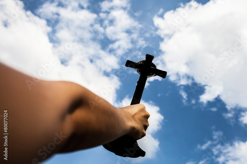 Silhouette of Hand holding cross in the sky, focus at the cross