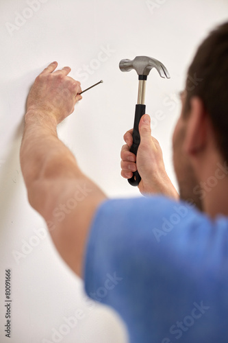 Fototapeta close up of man with hammer hammering nail in wall