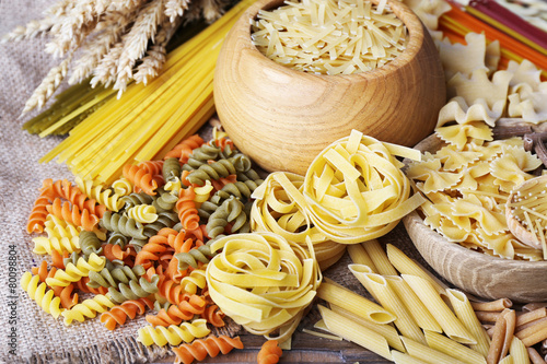 Different types of pasta with wheat on wooden table background
