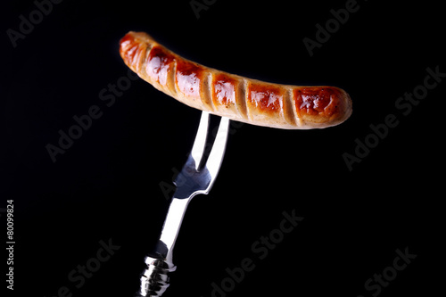 Grilled sausage on fork on black background