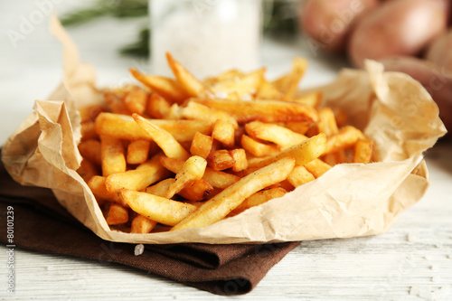 Tasty french fries on paper napkin, on wooden table background