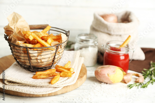 Tasty french fries in metal basket on color wooden background