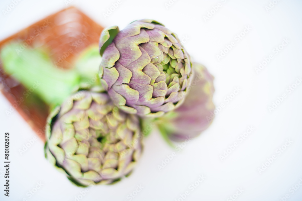 Fototapeta premium Bunch of three artichokes in basket on white background