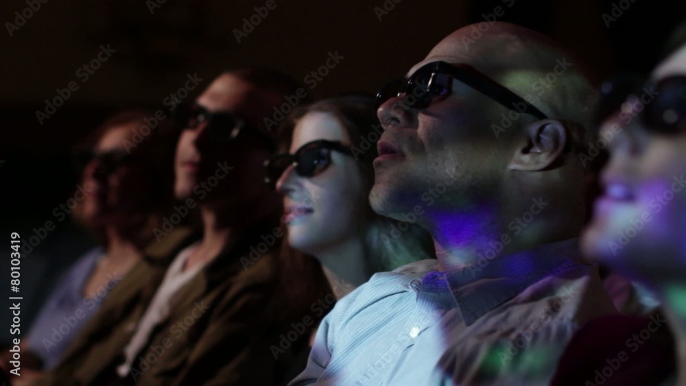 Young man watching a 3D movie with a group of friends. Focus on him with a small dolly move and projections on his face. Young man watching a 3D movie with a group of friends. Focus on him with a small dolly move and projections on his face.