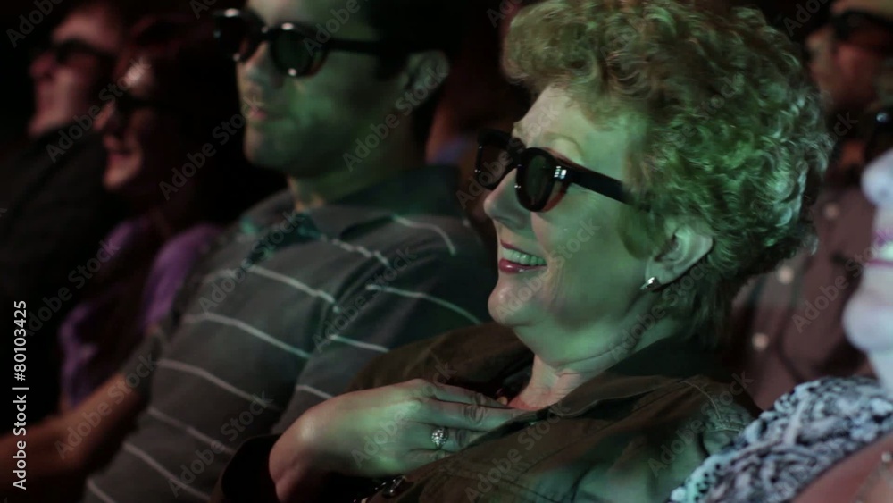 Mature woman gets excited as she watches a 3D movie. Focus on her with a small dolly move and projections on her face. Mature woman gets excited as she watches a 3D movie. Focus on her with a small dolly move and projections on her face.