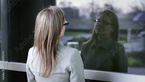 Businesswoman breathes a sigh of relief while reflecting on her day in the window of a modern office building.