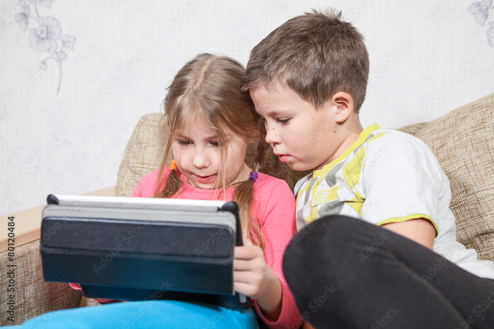 Sister and brother have fun with tablet pc while sitting on sofa Sister and brother have fun with tablet pc while sitting on sofa