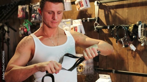 Muscular man in a vest holding leather whip at wooden room