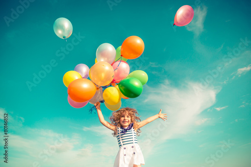 Child jumping with toy balloons in spring field