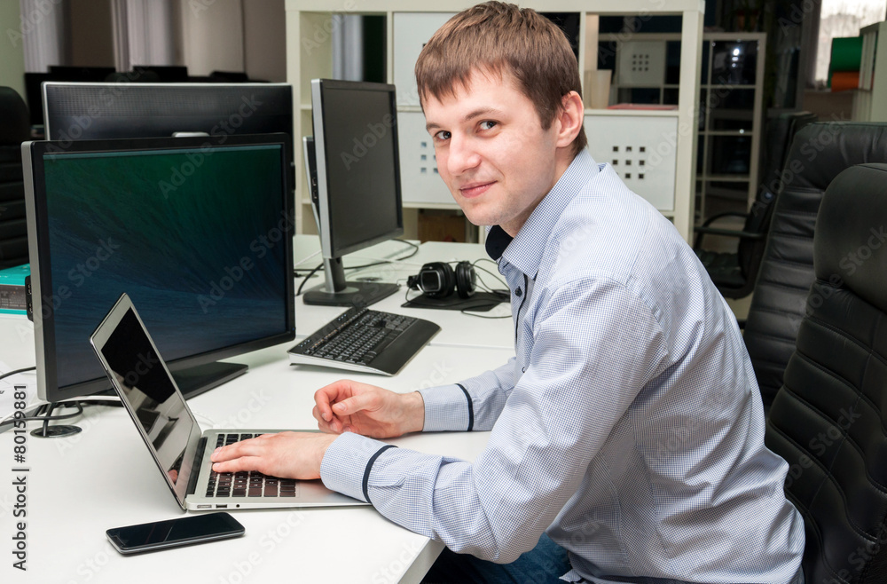 Young handsome happy man with computer in the office.