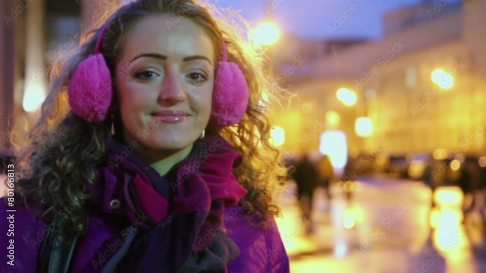 Girl in fury headphones smiles and holds head by hands on street Girl in fury headphones smiles and holds head by hands on street