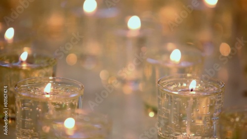 Rows of many candles burn in glasses, closeup view in dark photo