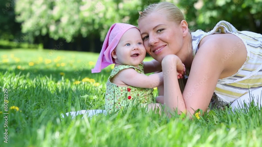 Young mother kisses her baby on grass at summer day Young mother kisses her baby on grass at summer day
