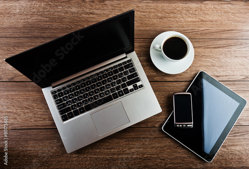 Office workplace with open laptop, tablet pc, phone and cup of c