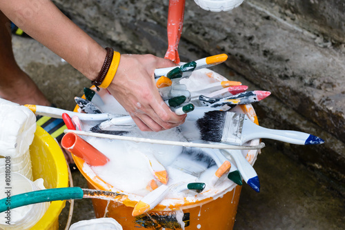 Close up of hand cleaning many paintbrushes.