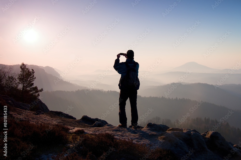 Tourist takes photos with smart phone of fogy hilly landscape