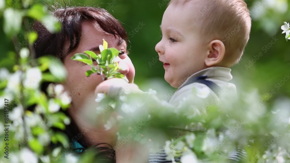 Mother and her little son play with branch of blooming tree Mother and her little son play with branch of blooming tree