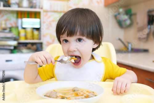 Toddler eats soup with meat balls at home kitchen