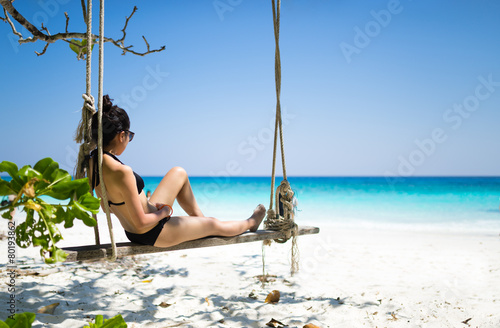 Bikini girl sitting on beach swing paradise