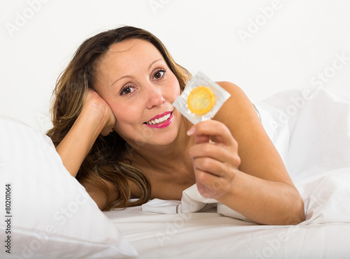 Adult woman holding condom in bed