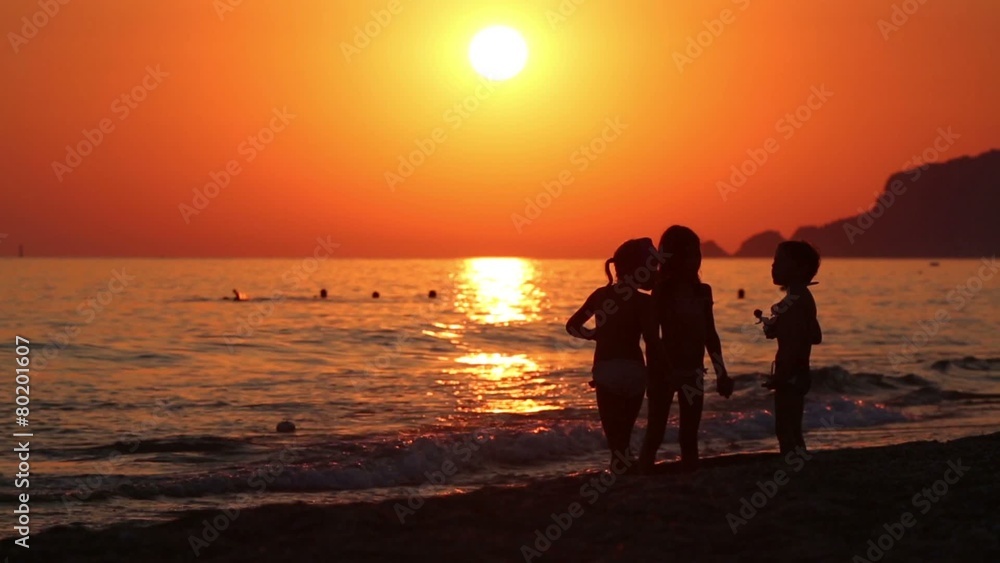 Three children talk at evening beach on red sunset Three children talk at evening beach on red sunset