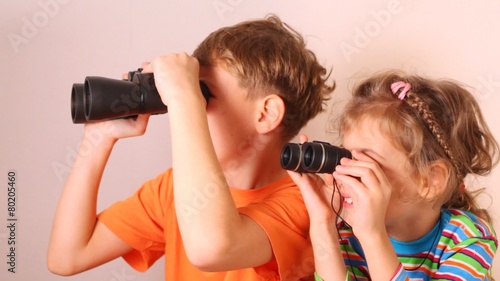 Cute little girl and boy looking through binoculars isolated on white photo