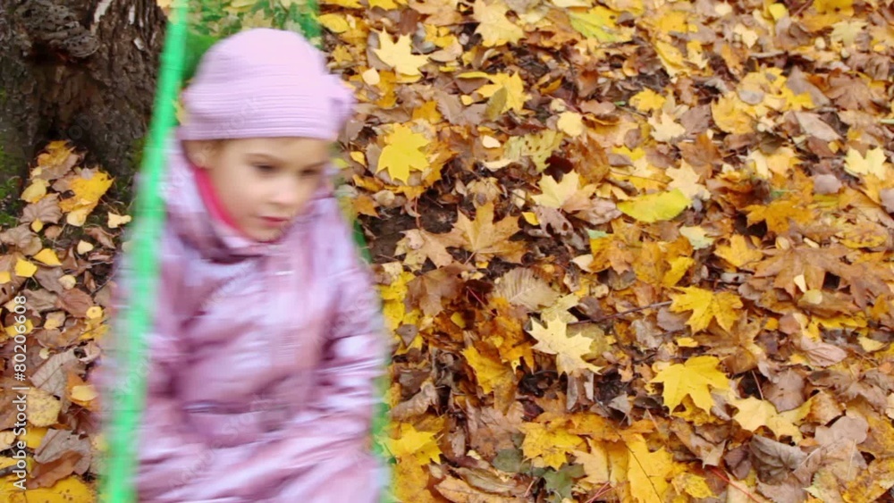 Little girl lies on hammock and sways under fallen leaves Little girl lies on hammock and sways under fallen leaves