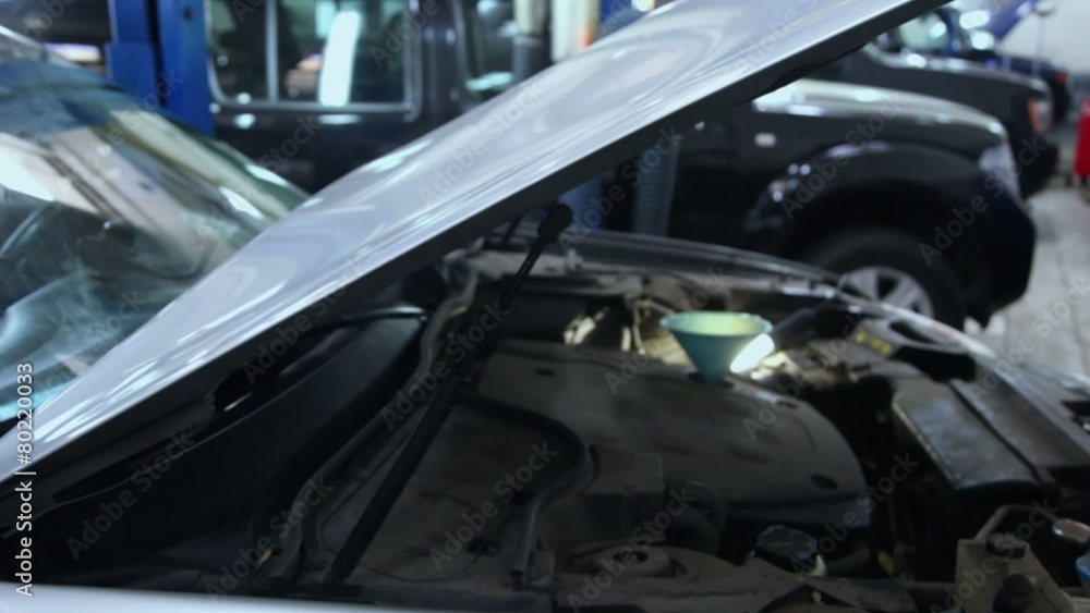 Funnel inserted in tank under open engine hood of car Funnel inserted in tank under open engine hood of car
