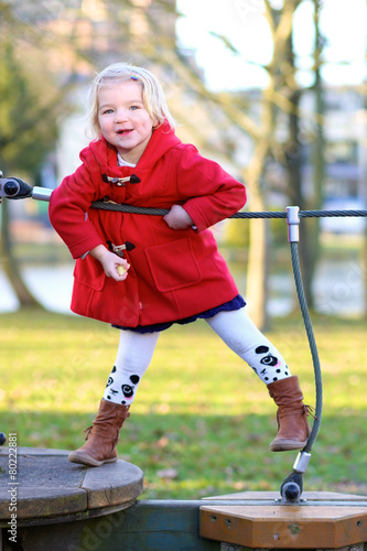 Little girl in red coat playing at the park in spring