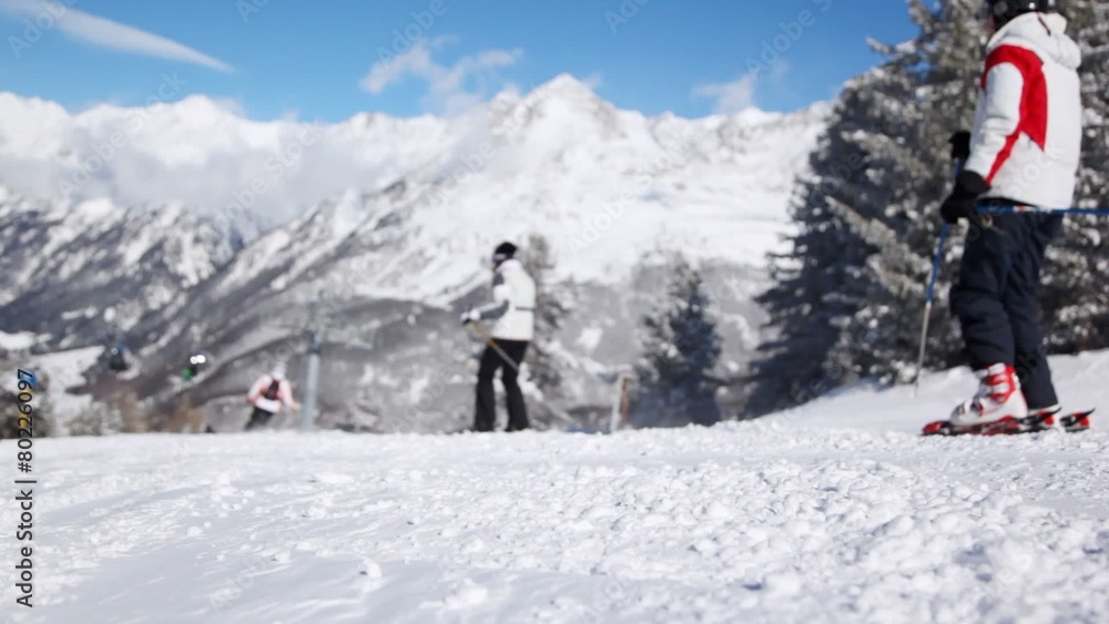Skiers go on mountain slope downwards near firs against blue sky Skiers go on mountain slope downwards near firs against blue sky