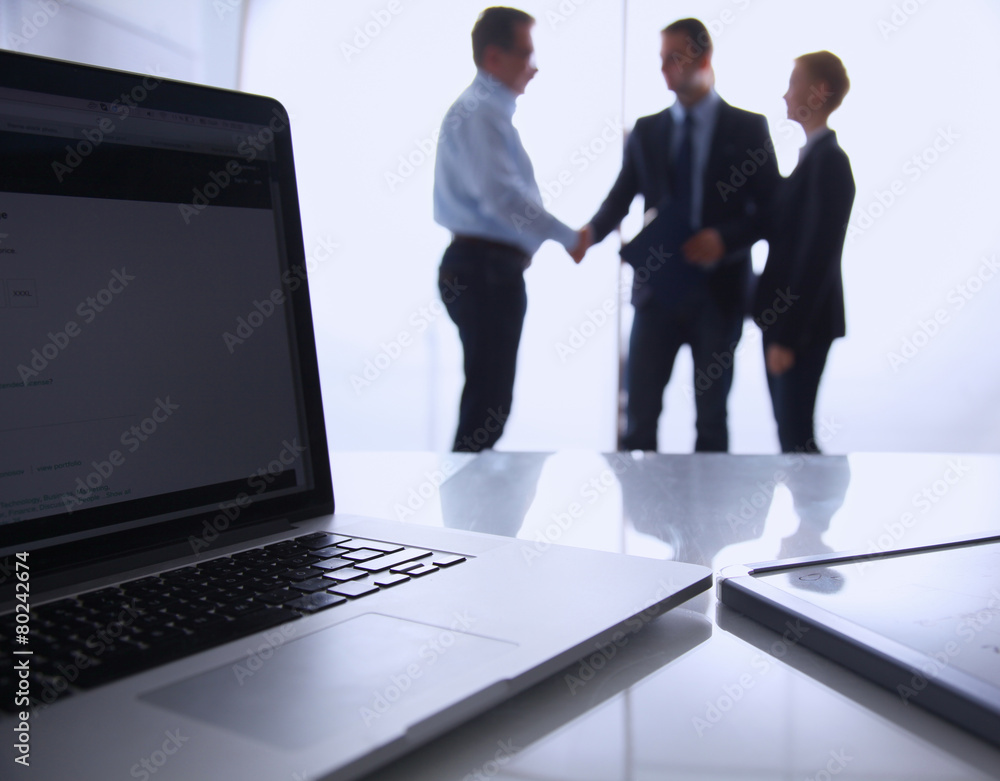Laptop  computer on  desk , three businesspeople standing in the