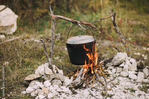 The image of a fire in the woods on which is brewed pot