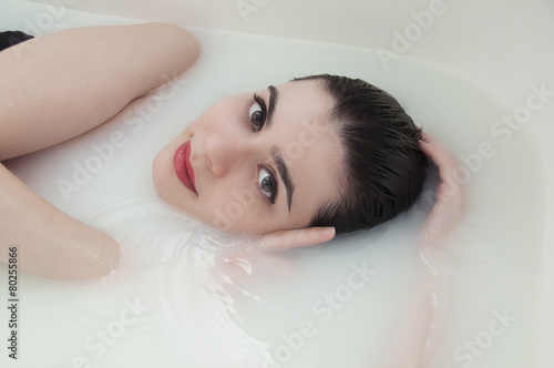 Fashion portrait of young woman floating in Spa filled with milk