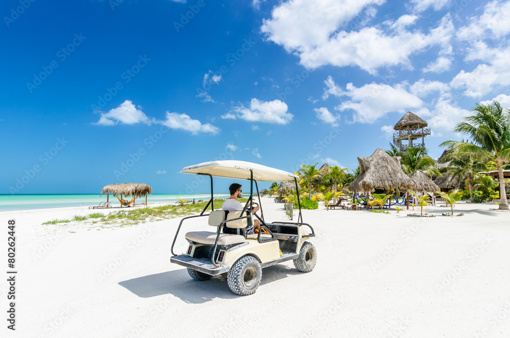 Young man driving golf cart along tropical sandy beach