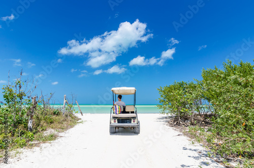 Young man driving on a golf cart at tropical white sandy beach