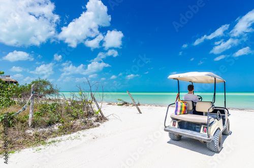 Fototapeta Naklejka Na Ścianę i Meble -  Young man driving on a golf cart at tropical white sandy beach