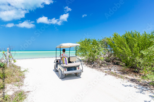 Young man driving on a golf cart at tropical white sandy beach