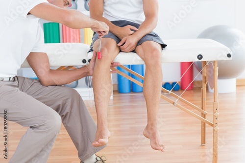 Fotografi Doctor checking reflexes of the knee of his patient