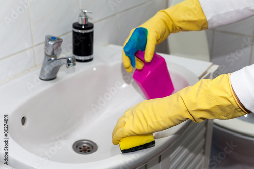 Woman cleaning sink and faucet with spray detergent.