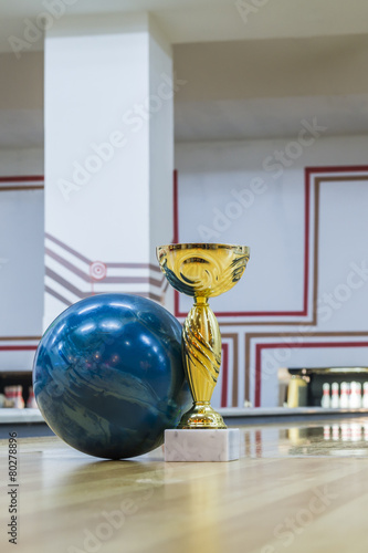 Closeup of blue bowling ball near golden trophy on the floor