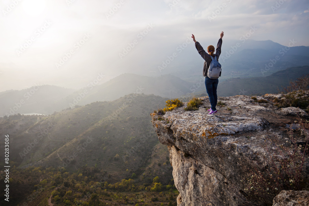 Young woman standing on cliff with outstretched arms