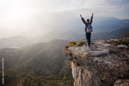 Young woman standing on cliff with outstretched arms