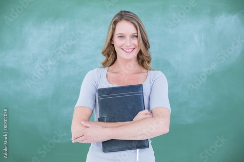Smiling teacher holding notebook in front of blackboard