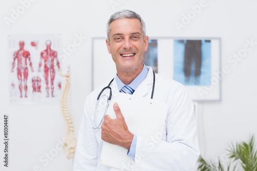 Happy doctor holding clipboard and smiling at camera